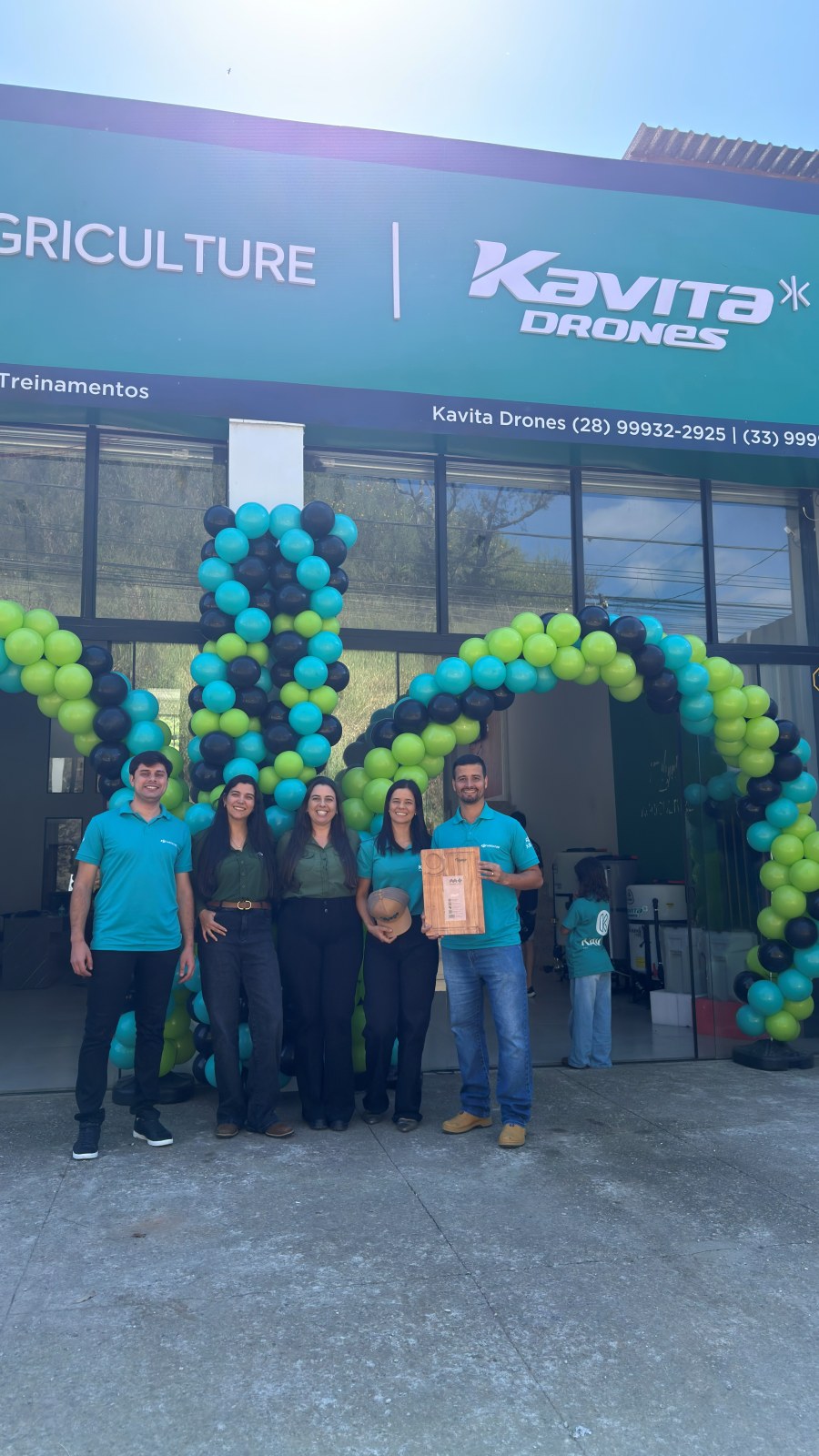 Equipe Kavita Drones com placa de premiação em frente à loja